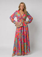 Multicolour swirl print maxi dress with ruffled V-neck and long sleeves, paired with a beige clutch