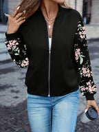 Woman wearing a black bomber jacket with pink floral-print sleeves, open over a white top and jeans