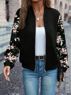 Front view of the black floral-sleeve bomber jacket zipped partway, worn with a belt and jeans