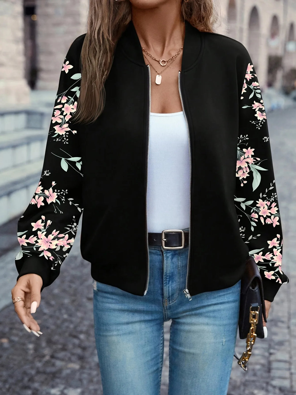 Front view of the black floral-sleeve bomber jacket zipped partway, worn with a belt and jeans