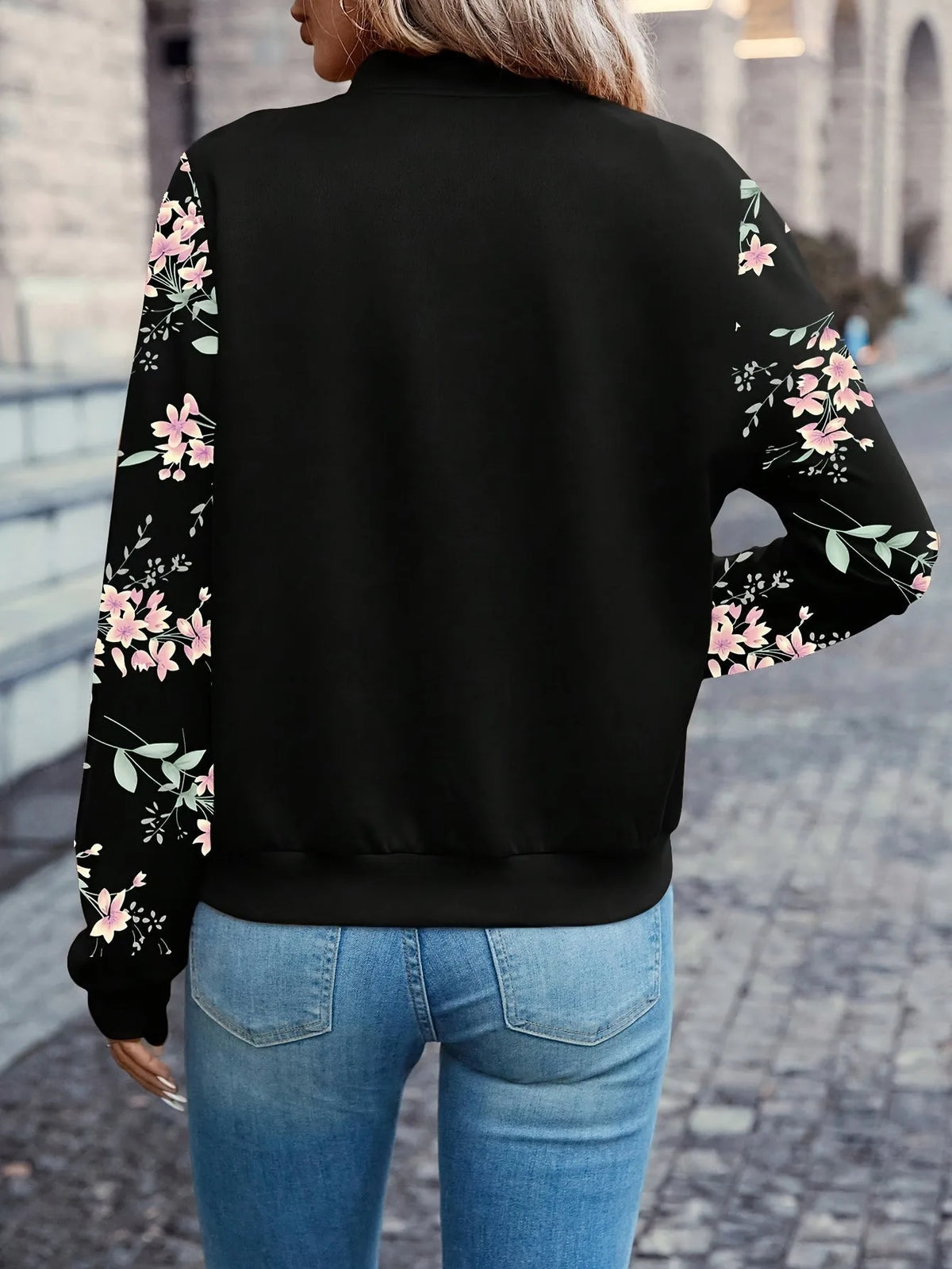 Back view showing the black bomber jacket's floral sleeve print and ribbed hem and collar