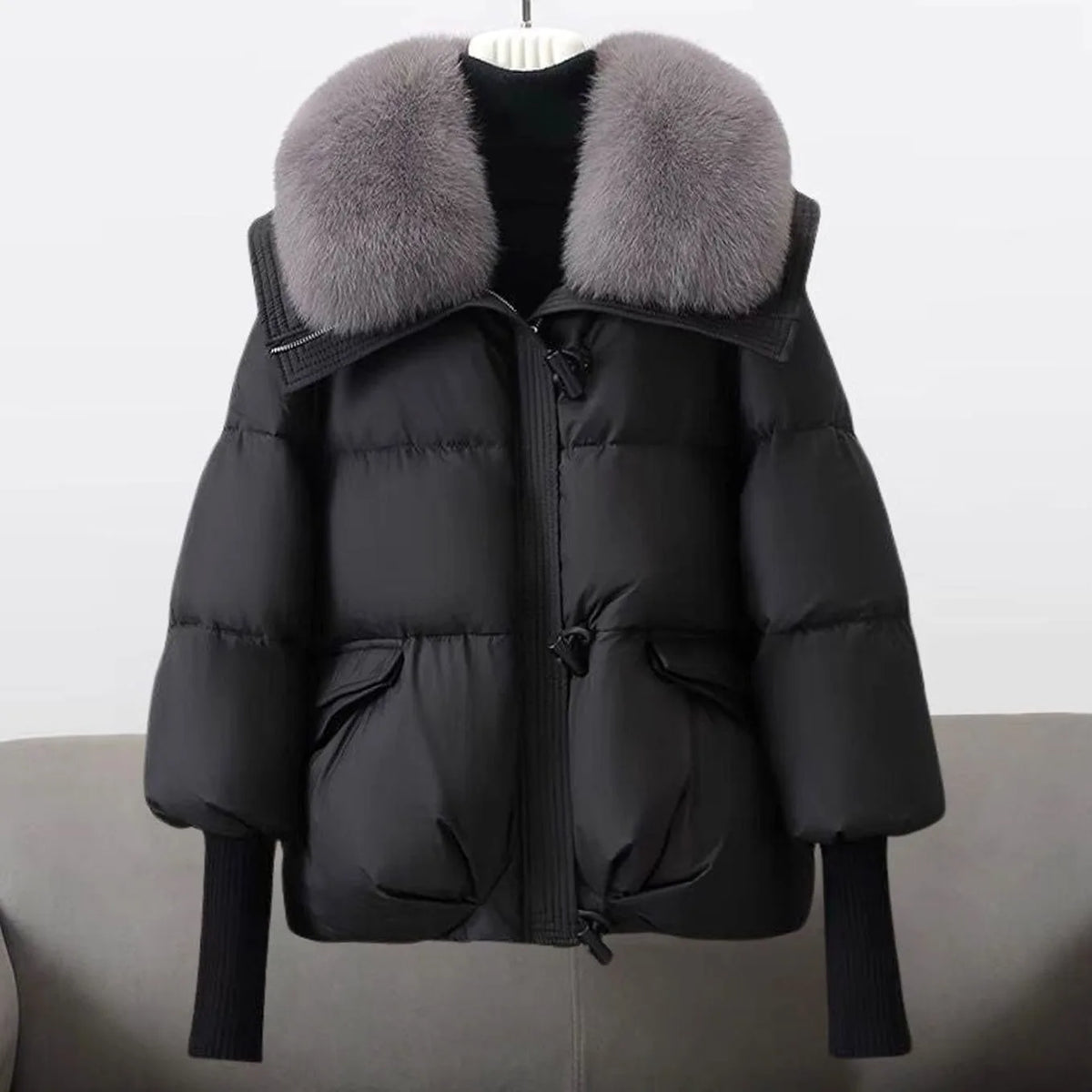 Front view of a black cropped puffer jacket with an oversized grey fox-style fur collar and ribbed knit cuffs