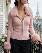 Model wearing a blush pink zip-front ribbed cardigan with matching faux fur collar and cuffs against a balcony backdrop
