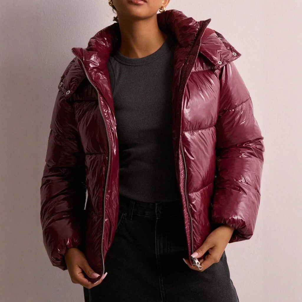 Front view of a burgundy high-shine puffer jacket worn open over a grey top, showing quilted panels and zip