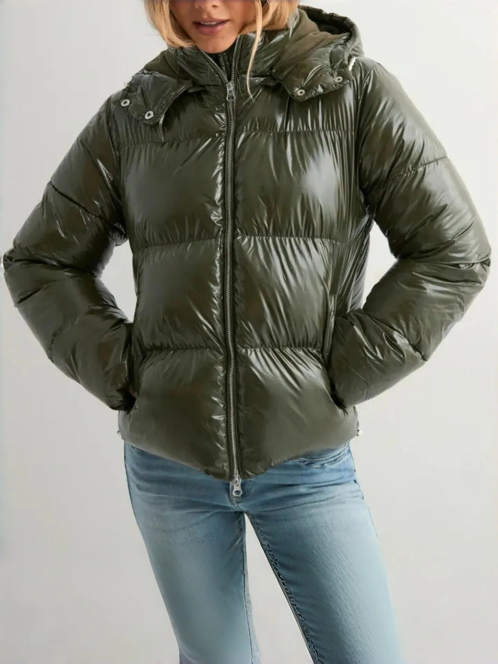 Front view of an olive green glossy puffer jacket with hood up, worn with light wash jeans