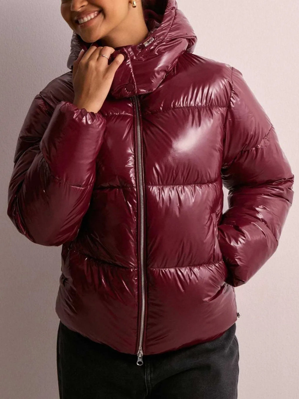 Close-up of the burgundy puffer jacket's hood and stand collar, worn with hand resting near the zip