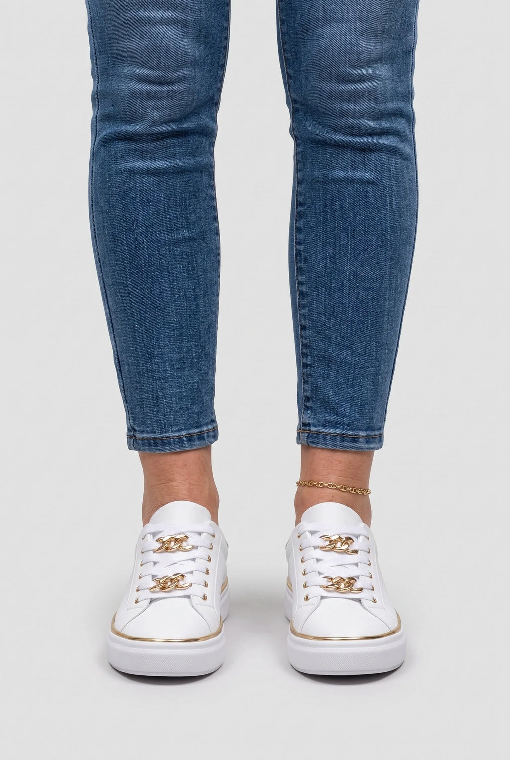 Front view of a person wearing white chain-lace trainers with cropped skinny jeans and a gold anklet