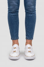 Front view of a person wearing white chain-lace trainers with cropped skinny jeans and a gold anklet