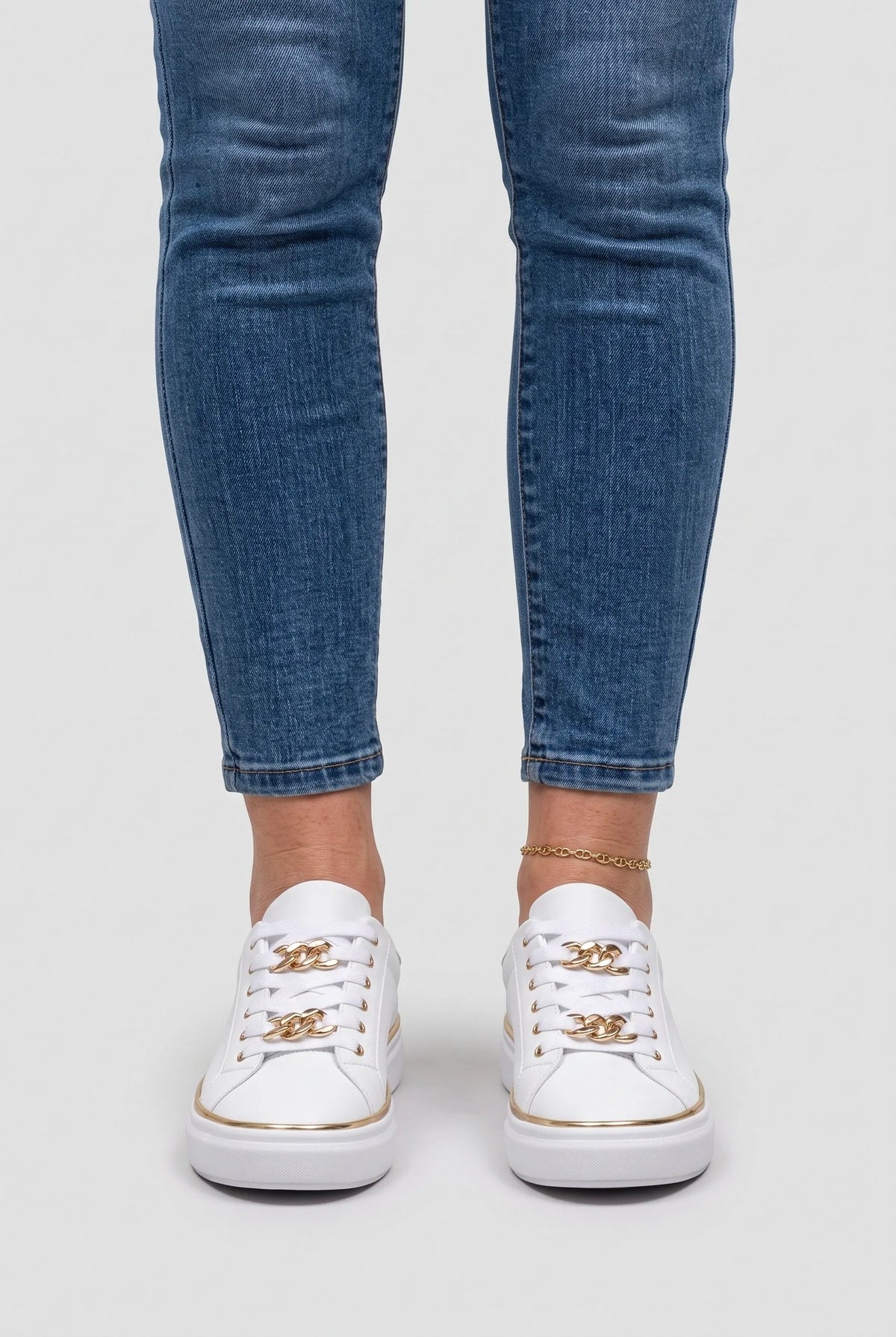 Front view of a person wearing white chain-lace trainers with cropped skinny jeans and a gold anklet