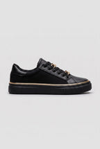 Side view of a black trainer with gold chain-link lace detail and a slim gold trim around the black sole
