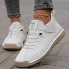 White leather trainers with tan stitched sole and touch-fastening strap shown on a paved street