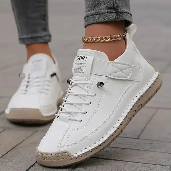 White leather trainers with tan stitched sole and touch-fastening strap shown on a paved street