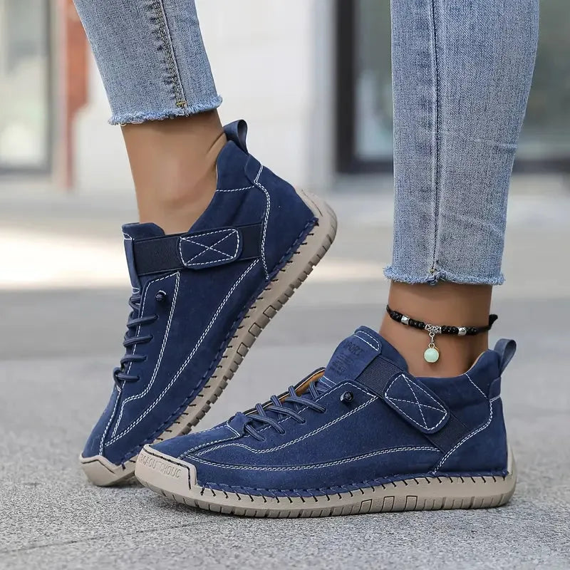 Navy suede trainers with contrast stitching and elastic side strap paired with denim jeans