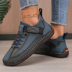 Close-up side profile of teal-blue leather trainers with visible hand-stitched seams and orange sole accent