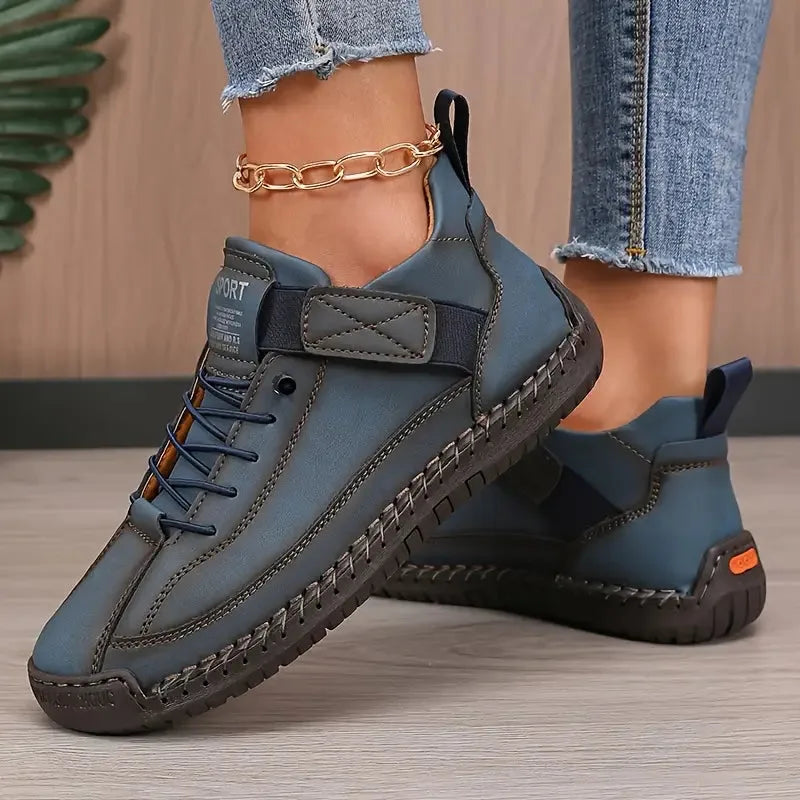 Close-up side profile of teal-blue leather trainers with visible hand-stitched seams and orange sole accent
