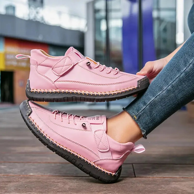 Pink leather trainers with contrast stitching and touch-fastening strap held up by hand