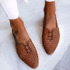 Brown woven leather flats with scalloped edge and lace-up vamp, captured close up on a textured stone surface
