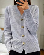 Grey knitted cardigan with V-neck and gold heart-shaped buttons, worn with ribbed cuffs visible