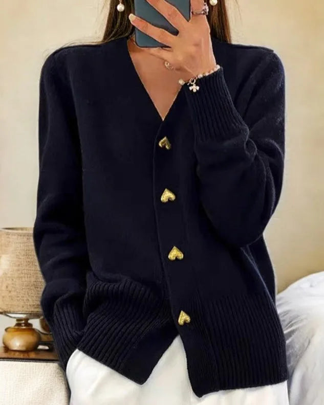 Navy knitted cardigan with gold heart-shaped buttons and relaxed V-neckline, worn over white trousers