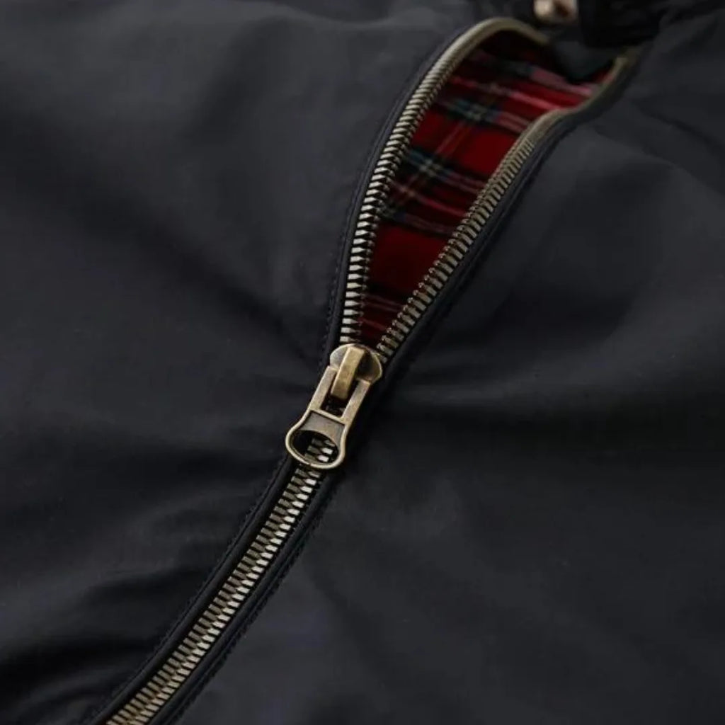 Close-up of brass zip pull against black fabric with red tartan lining peeking through