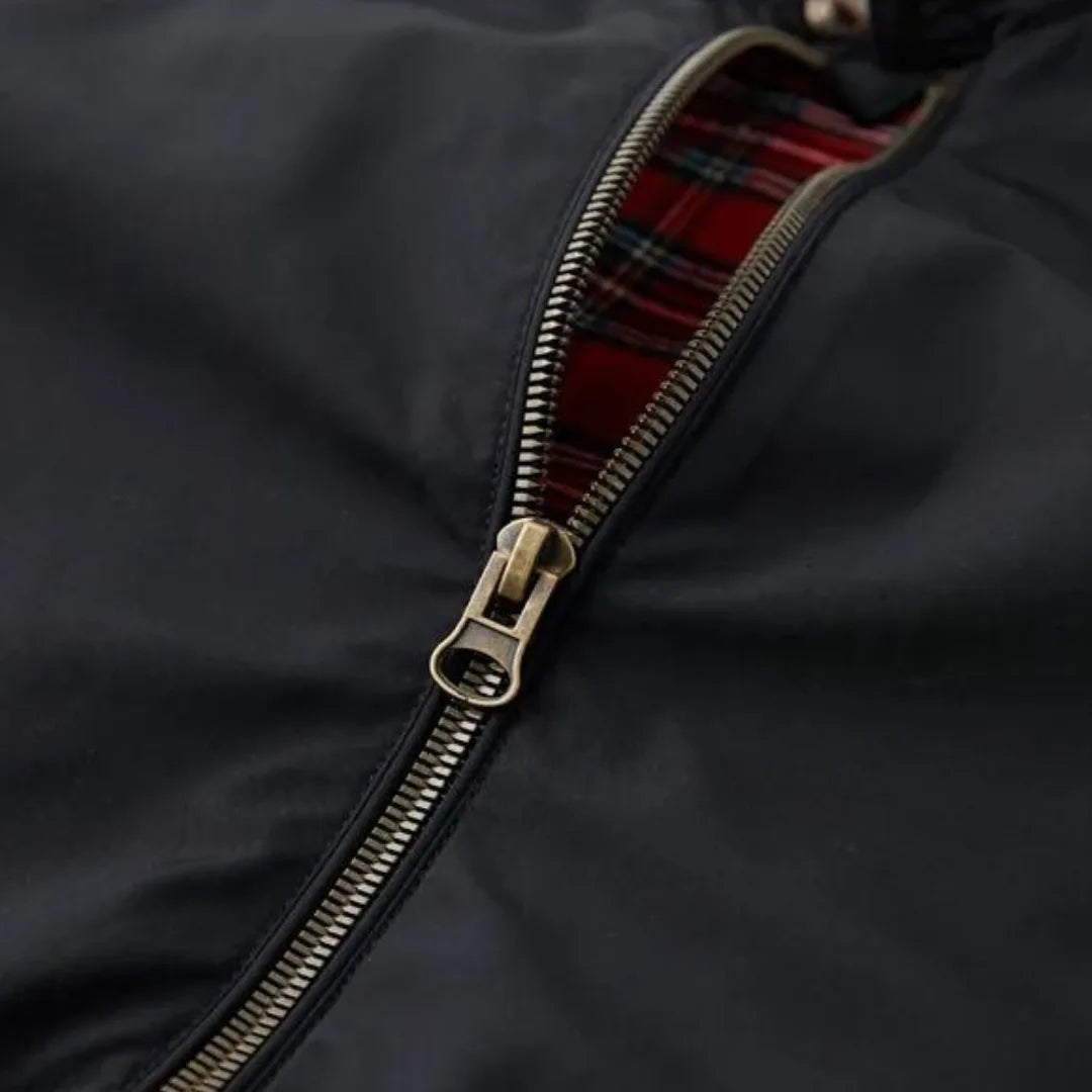 Close-up of brass zip pull against black fabric with red tartan lining peeking through