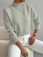 Sage green high neck jumper worn with layered silver necklaces, close view of ribbed collar and soft knit texture.