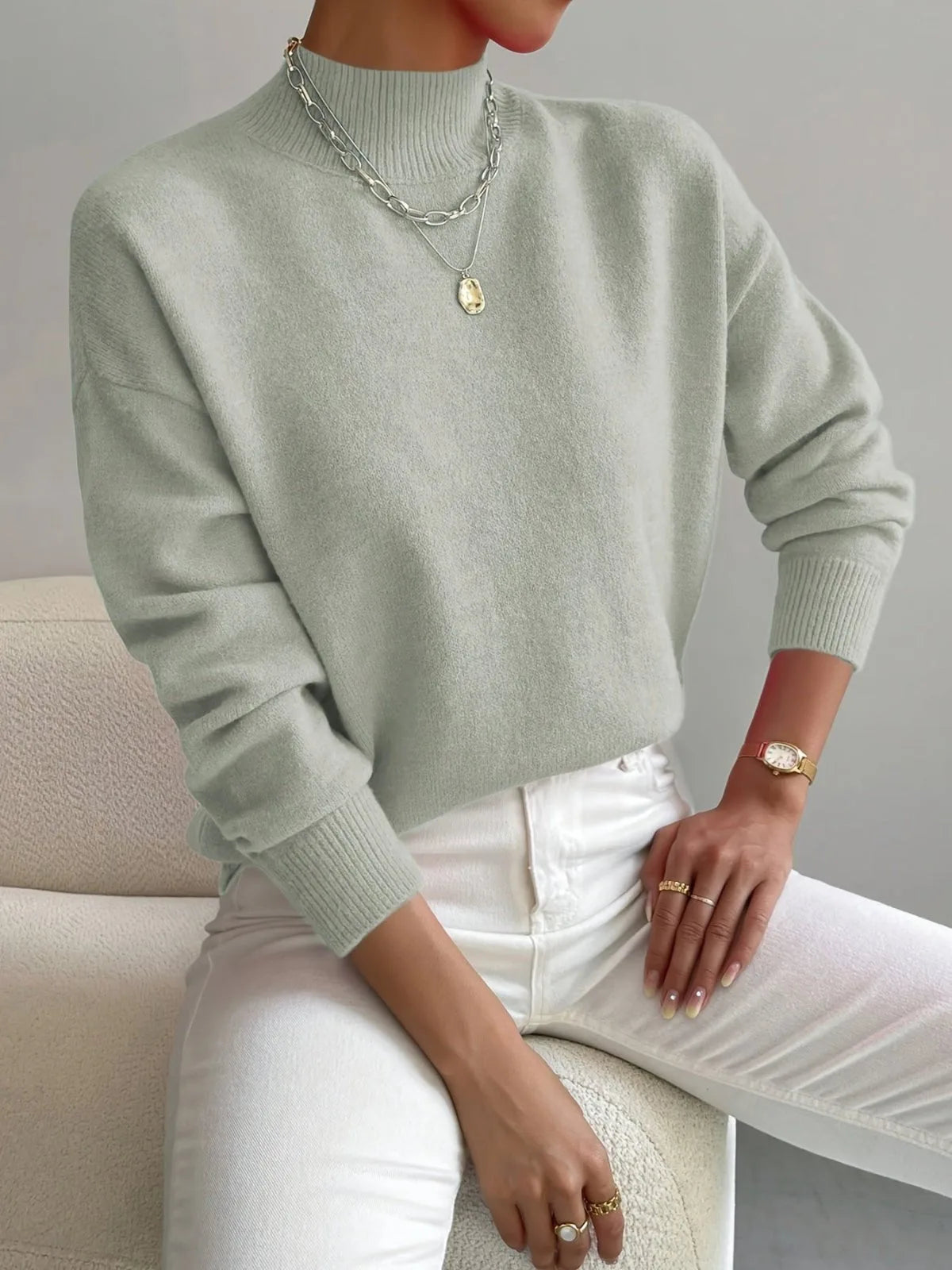 Sage green high neck jumper worn with layered silver necklaces, close view of ribbed collar and soft knit texture.