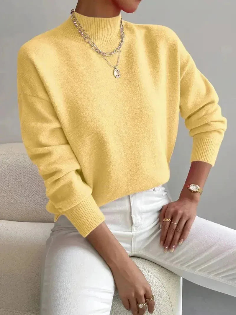 Soft yellow high neck jumper with relaxed sleeves, shown with layered necklace and white trousers.