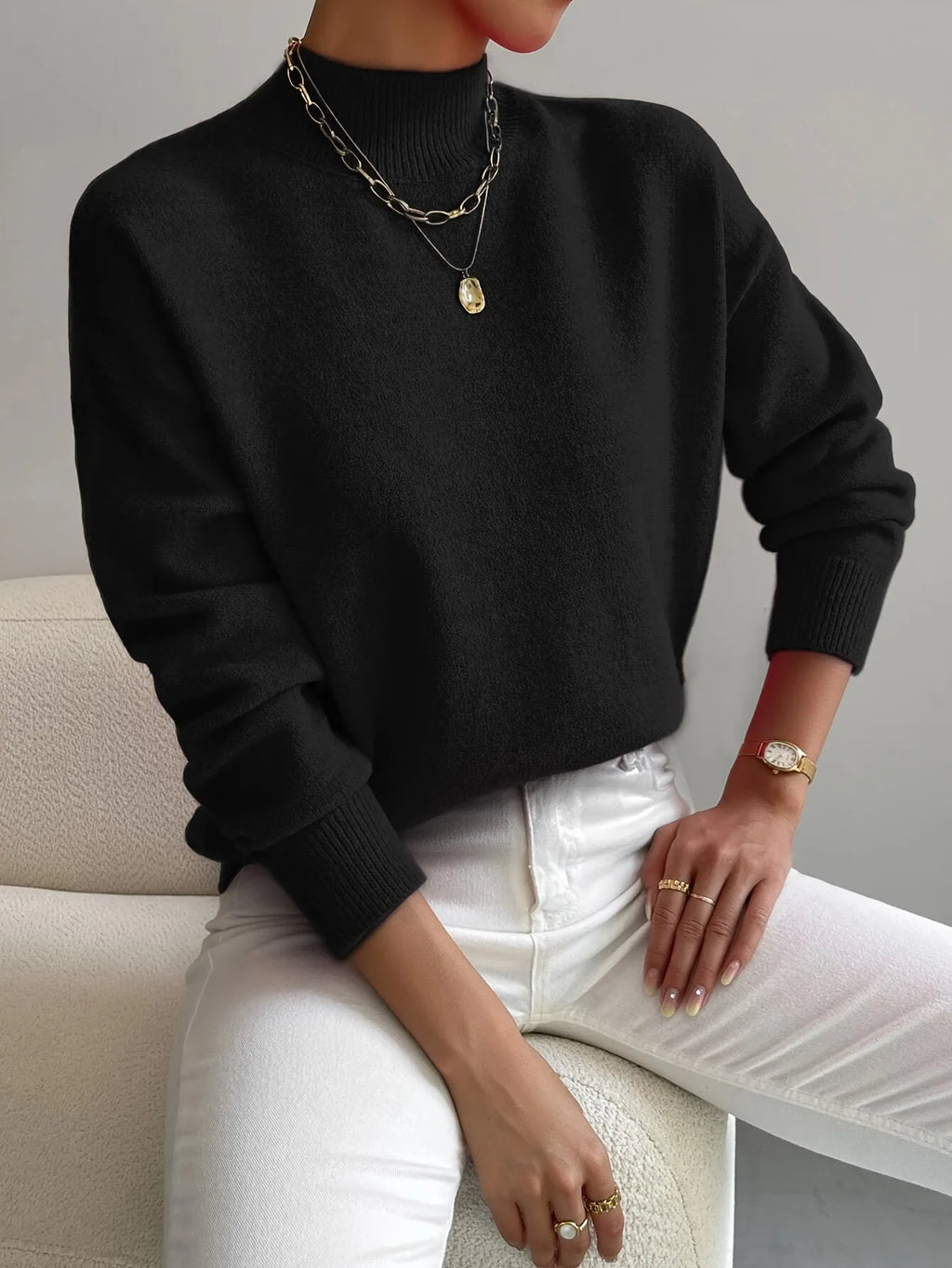 Black high neck jumper with mock neck and ribbed cuffs, styled with layered gold and silver necklaces.