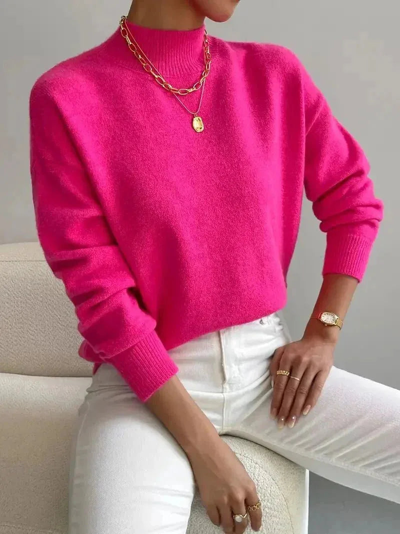 Bright pink high neck jumper with ribbed trim, paired with gold chain necklace and white trousers.