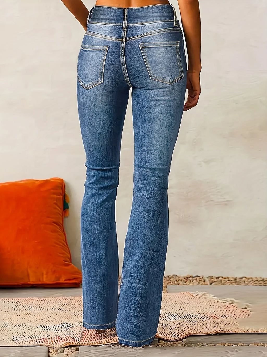 Back view of mid-blue flared jeans showing high waist, curved yoke and topstitched patch pockets