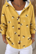 Close-up of a mustard yellow hooded jacket printed with a playful bee and dotted trail pattern, worn with white trousers