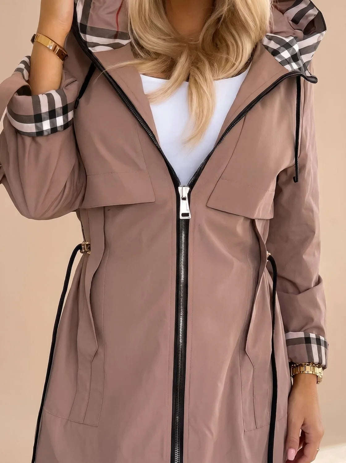 Close-up of the mocha brown trench coat showing the checked hood and cuff lining, zip pull, and drawstring waist toggles