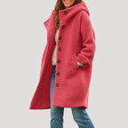 Rose pink hooded wool-blend coat with wooden button placket, worn open over a cream jumper and jeans