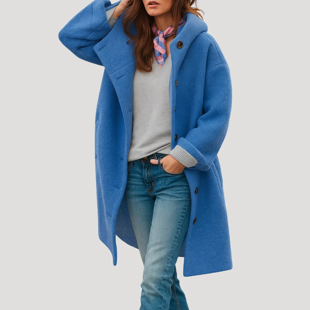 Blue hooded wool coat worn open with hand in pocket, paired with a grey jumper and denim trousers