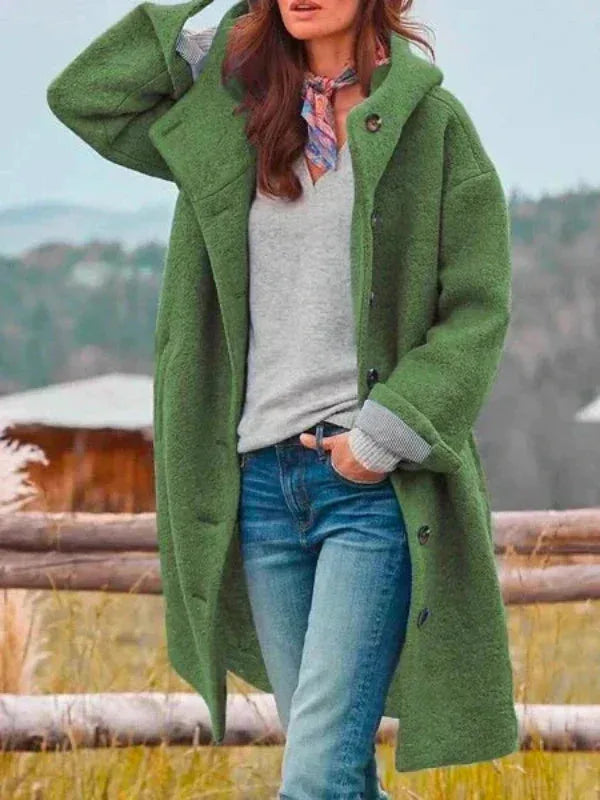 Woman in a green hooded wool coat with buttoned placket, hand raised adjusting the hood
