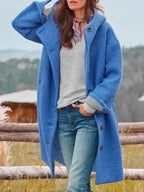 Front view of a blue hooded wool coat worn open over a grey jumper and jeans