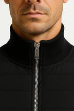 Close-up of the stand collar, ribbed knit trim and silver zip pull on the black quilted jacket