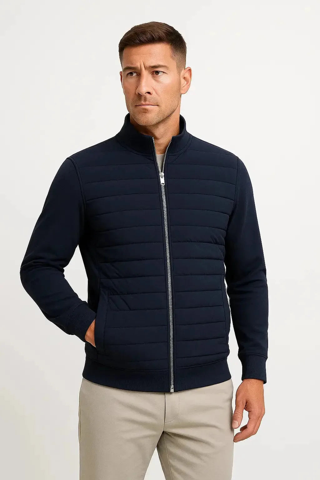 Front view of a man wearing the jacket in navy with quilted body, knitted sleeves and stand collar, hand in pocket