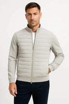 Front view of a man wearing the jacket in light grey with quilted front, ribbed collar and hand in pocket