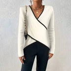 Woman wearing an ivory wrap-style jumper with black trim detailing, layered with a chain-strap shoulder bag.