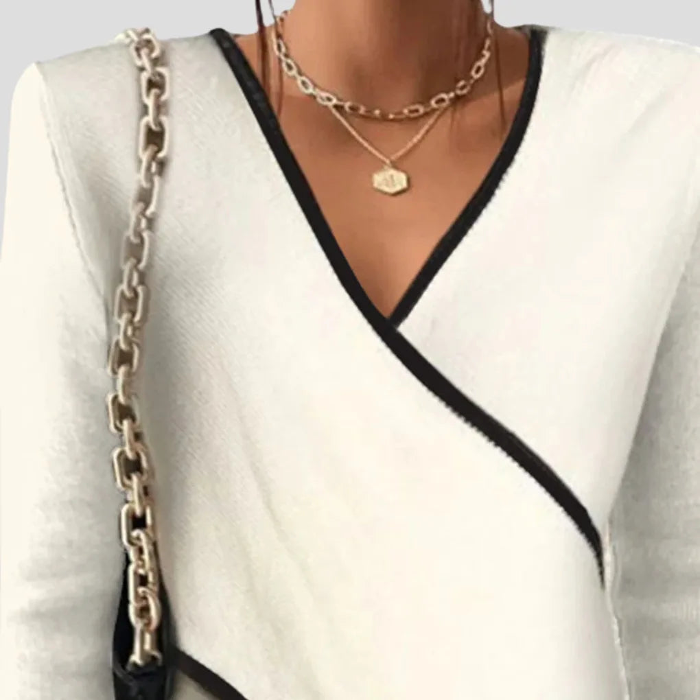 Close-up of the asymmetric V-neckline showing black contrast piping over soft ivory knit fabric.