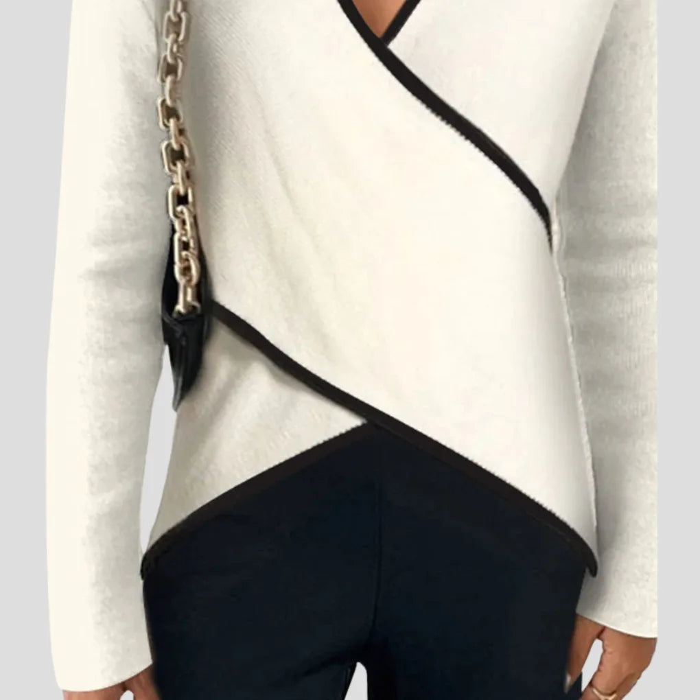 Side view of the wrap hem detail, showing the crossover black trim against the ivory knit and black trousers.