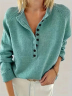 Close-up front view of a woman wearing an emerald green knit jumper with black button placket and folded collar