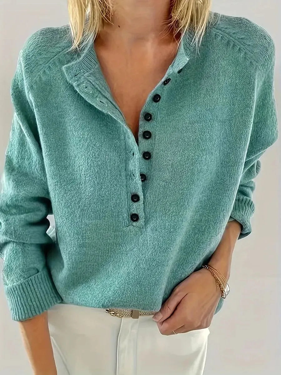 Close-up front view of a woman wearing an emerald green knit jumper with black button placket and folded collar