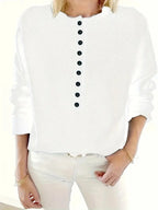 Detail shot of the black button placket and folded collar on a knit jumper worn with white trousers