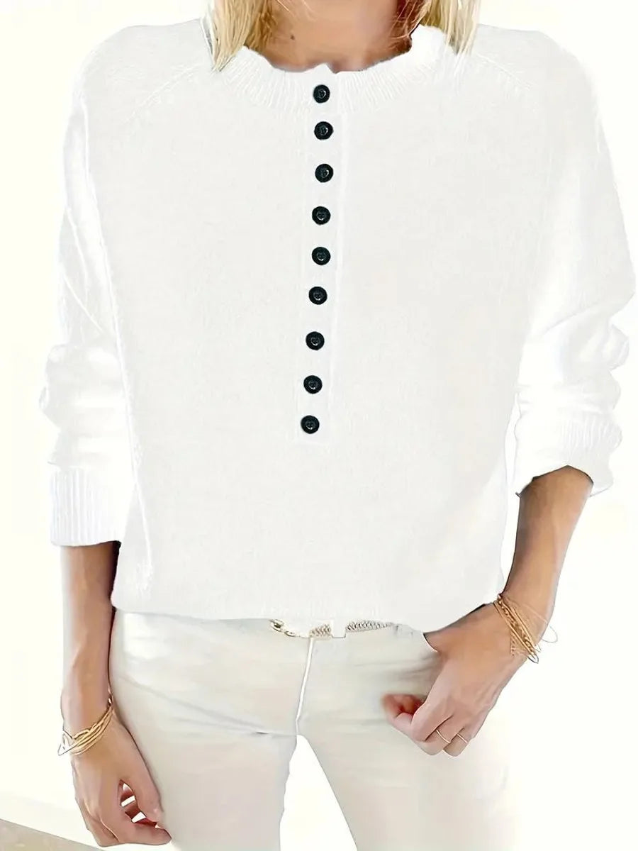 Detail shot of the black button placket and folded collar on a knit jumper worn with white trousers