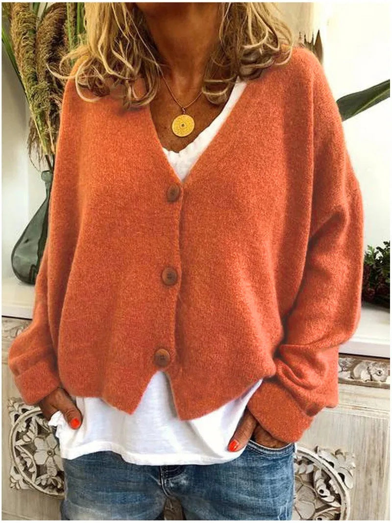 Close-up of a burnt orange knitted button-front cardigan worn open over a white top, styled with blue jeans