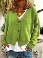 Green knitted cardigan with wooden-style buttons, V-neck cut, worn over a white top and denim jeans