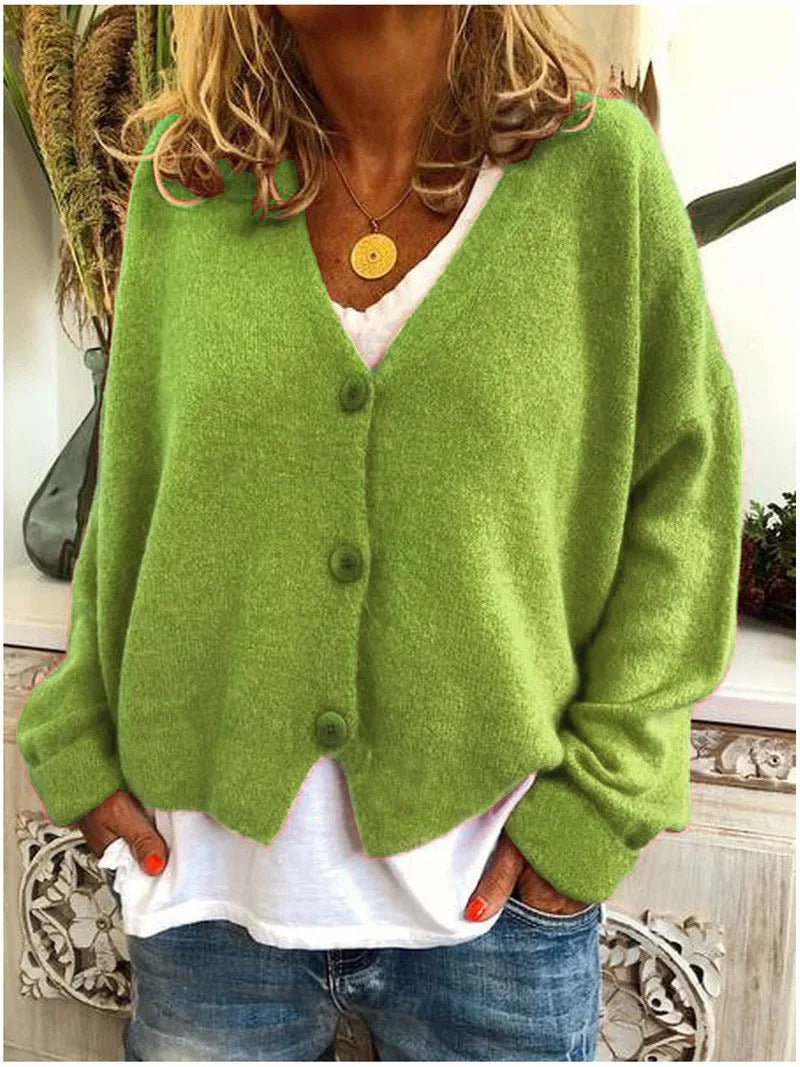 Green knitted cardigan with wooden-style buttons, V-neck cut, worn over a white top and denim jeans